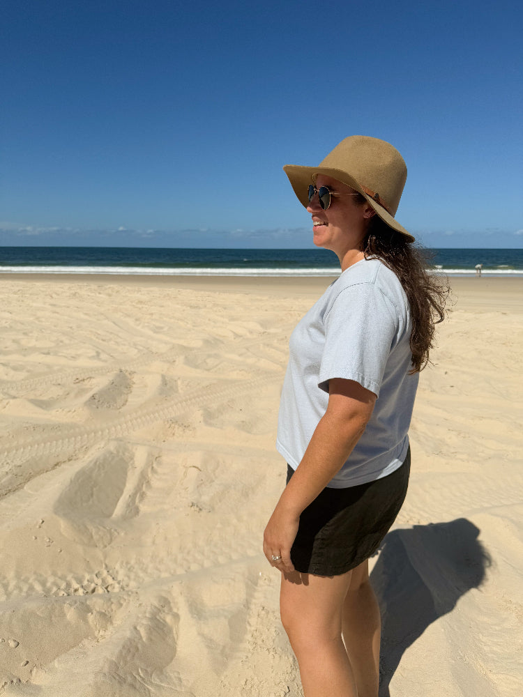 Woman wearing Australian made - The Vera in dusty blue Good Earth Cotton while at the beach walking on sand. 