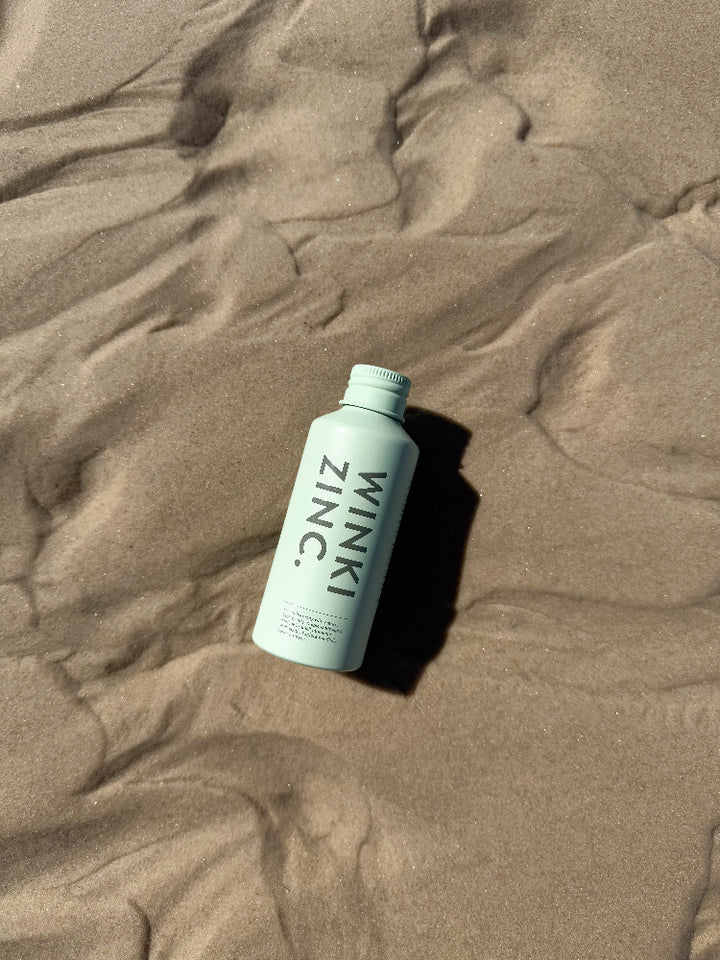 Bottle of Winki Zinc natural face cleanser laying on sandy beach