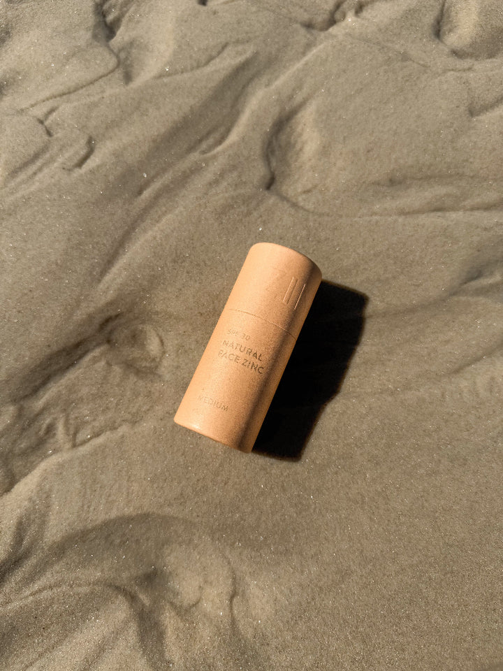 SPF 30 Natural face zinc in medium skin shade laying on sand at beach