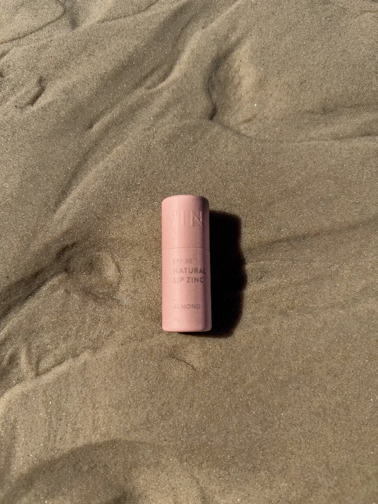 Winki Zinc natural lip zinc in almond shade laying on the sand. 