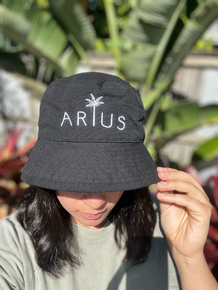 Black bucket hat made from recycled cotton and recycled polyester. Features a white embroidered logo. Available in sizes S/M and M/L. Ethically produced with certifications and shipped in eco-friendly packaging.
