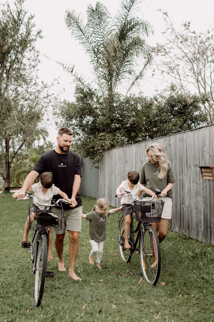 Family wearing natural, ethical, organic cotton t-shirts in multiple colours while riding bikes together.