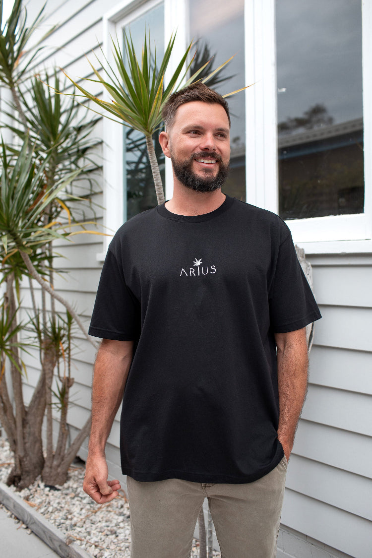 Man wearing organic cotton unisex t-shirt in black with palm tree logo in white. 