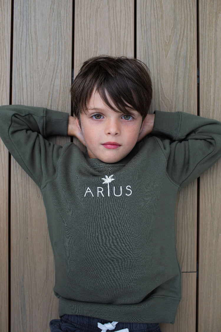 Organic cotton kids jumper ethically made with centred logo worn by child laying on deck. 