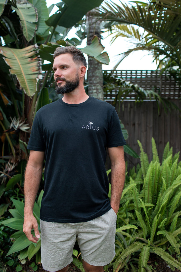 Man wearing unisex organic cotton t-shirt in black with small front palm tree logo. 