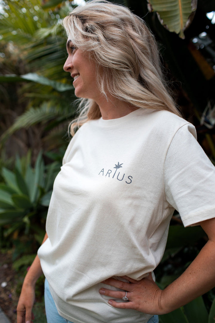 Woman wearing unisex organic cotton Arius t-shirt in natural with palm tree logo. 